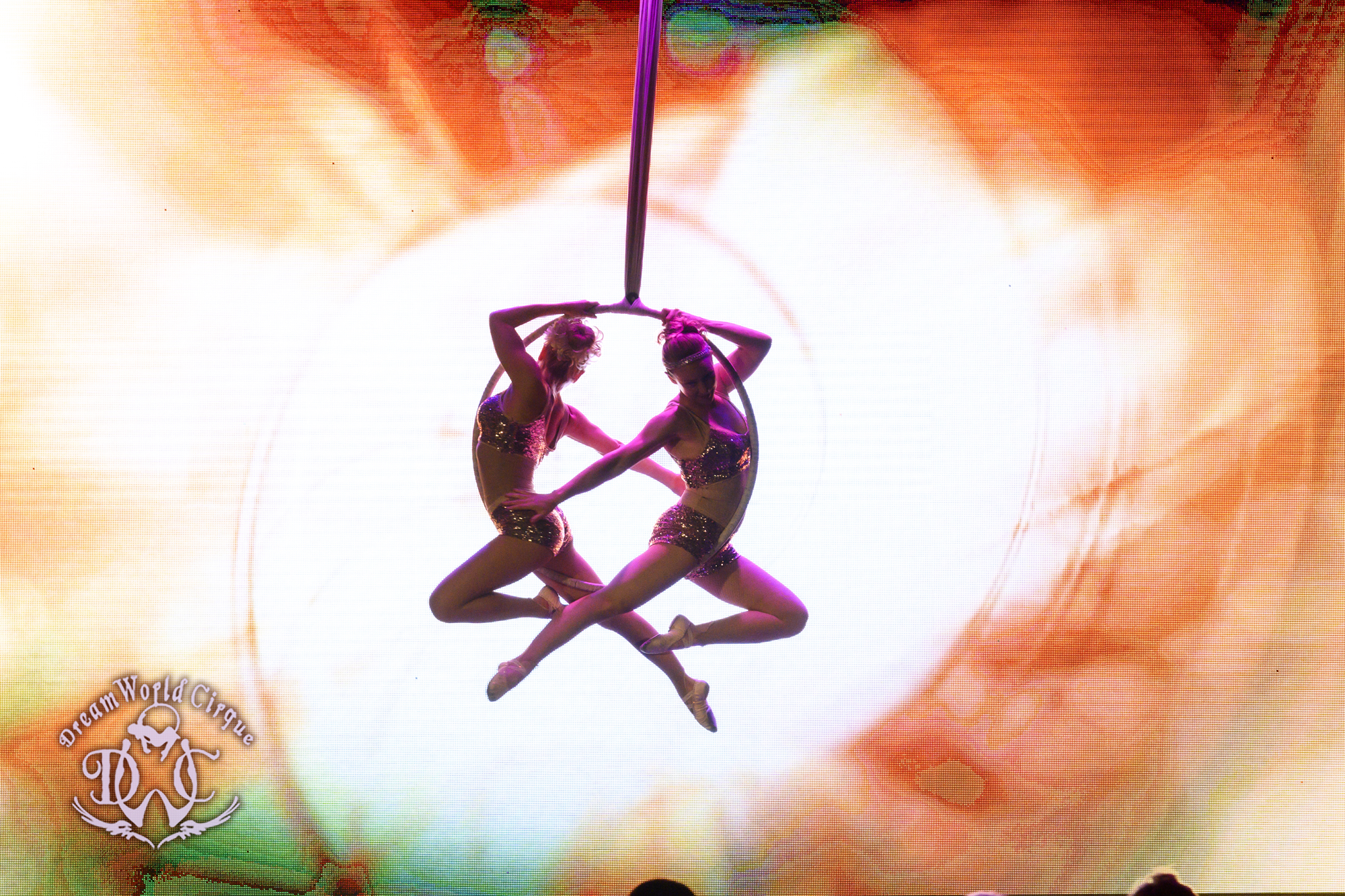 Two Aerialists glide around each other through the air on their aerial hoop, making beautiful shapes