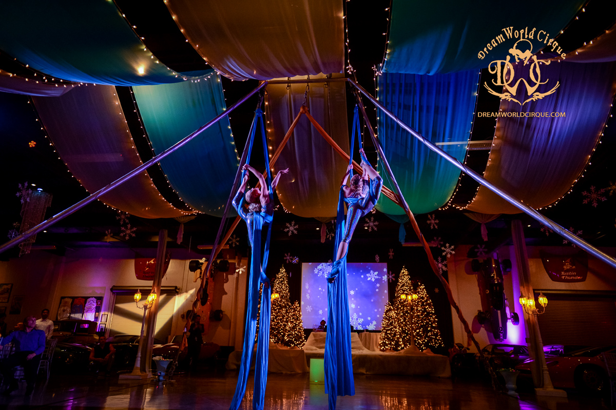 two beautiful female aerialists perform intricate maneuvers in turquoise silks in a beautifully draped room for a corporate event