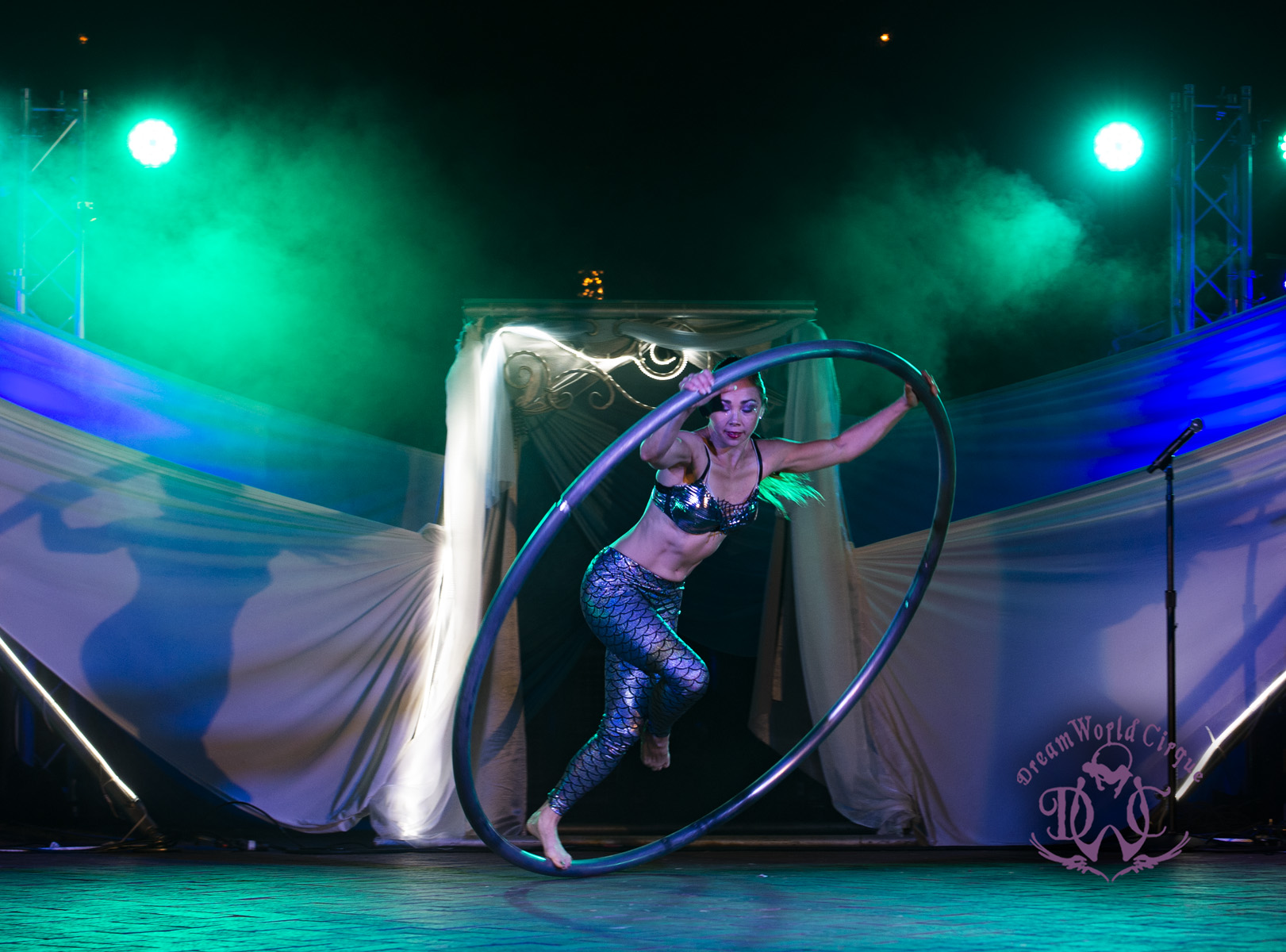 Cyr Wheel Performer in large circle with mermaid colors and cool LED Scene behind her